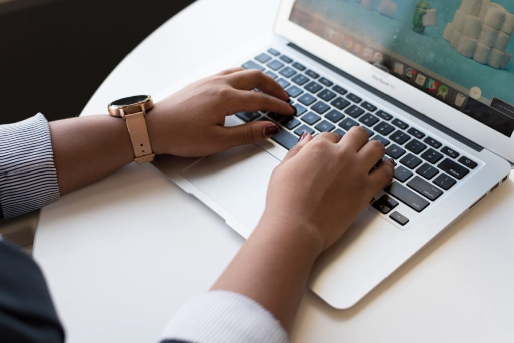 Person typing on a laptop at a white table, wearing a watch and striped shirt sleeves—highlighting potential ergonomic risk factors in everyday work settings.