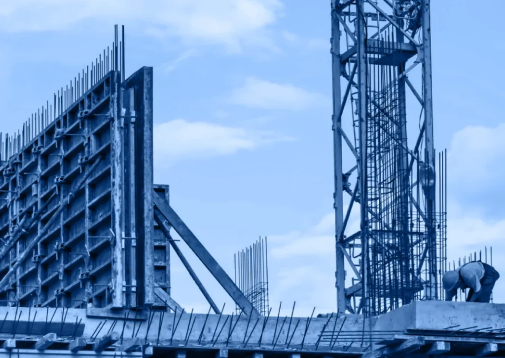 A construction site with steel reinforcement bars, concrete formwork, and scaffolding showcases the framework of a home under construction against a partly cloudy sky.