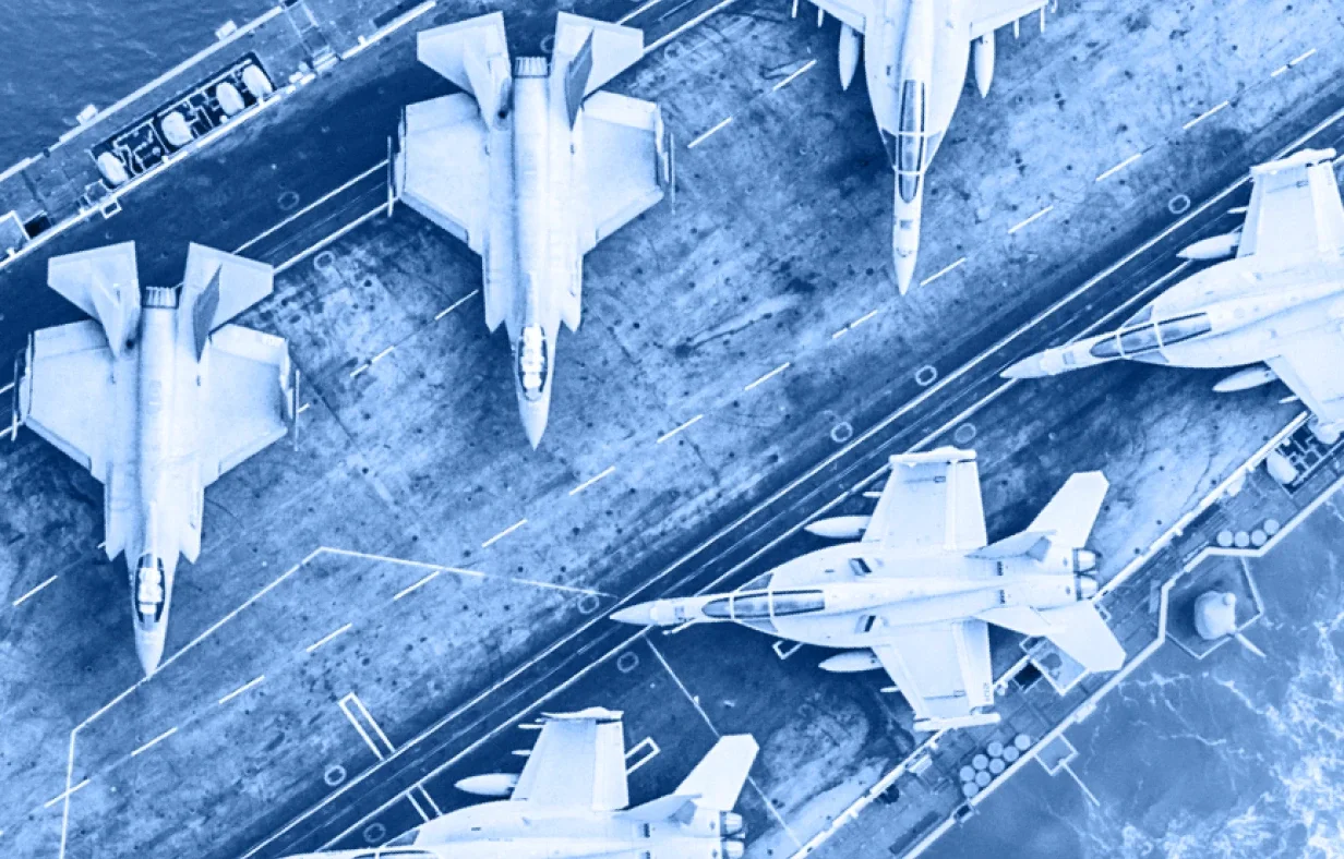 Aerial view of five fighter jets parked on the deck of an aircraft carrier at sea, showcasing the impressive scale of this floating home of naval aviation and military industry, with the ocean visible along the ship's edge.
