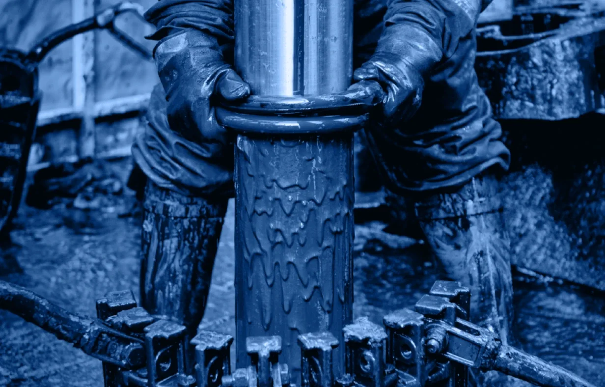 A worker in protective gloves holds a large metal pipe covered in oil, with oily machinery parts and bolts visible below—all tinted in blue tones, reflecting the vital work done within the Industry Accordion home.